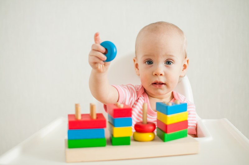 Little girl plays with an educational toy - a multi-colored wooden pyramid.