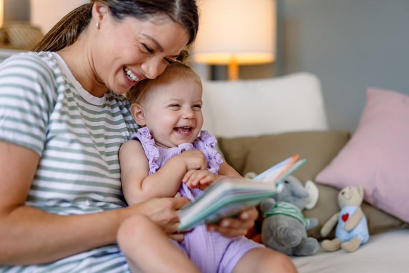 Mother and child laugh together while reading book.