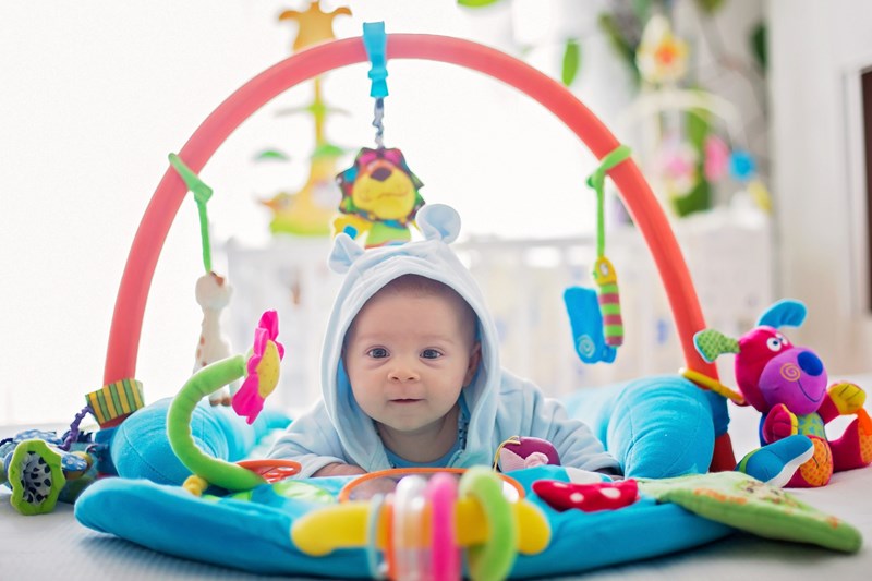 Cute baby boy on colorful gym, playing with hanging toys at home