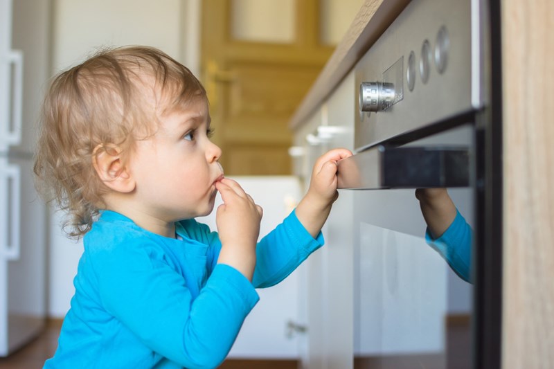 Small and curious child playing with the knobs of the oven in the kitchen. Danger for unattended children